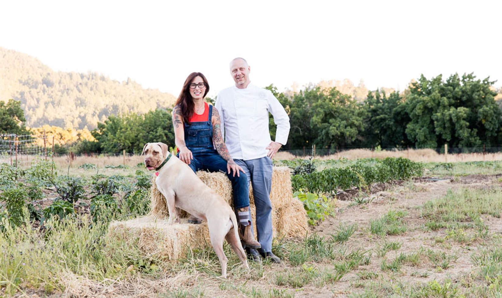 a man and a woman with a dog sitting in a barn