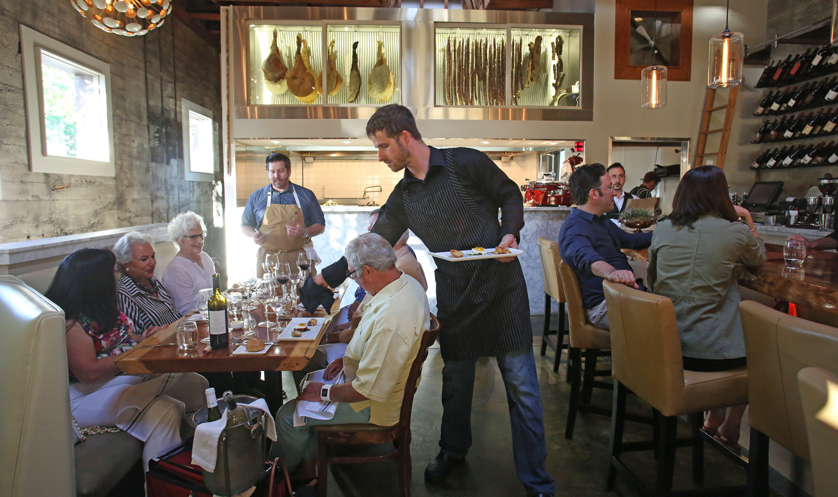 a crew serving meal to a group of old people in the table with wine