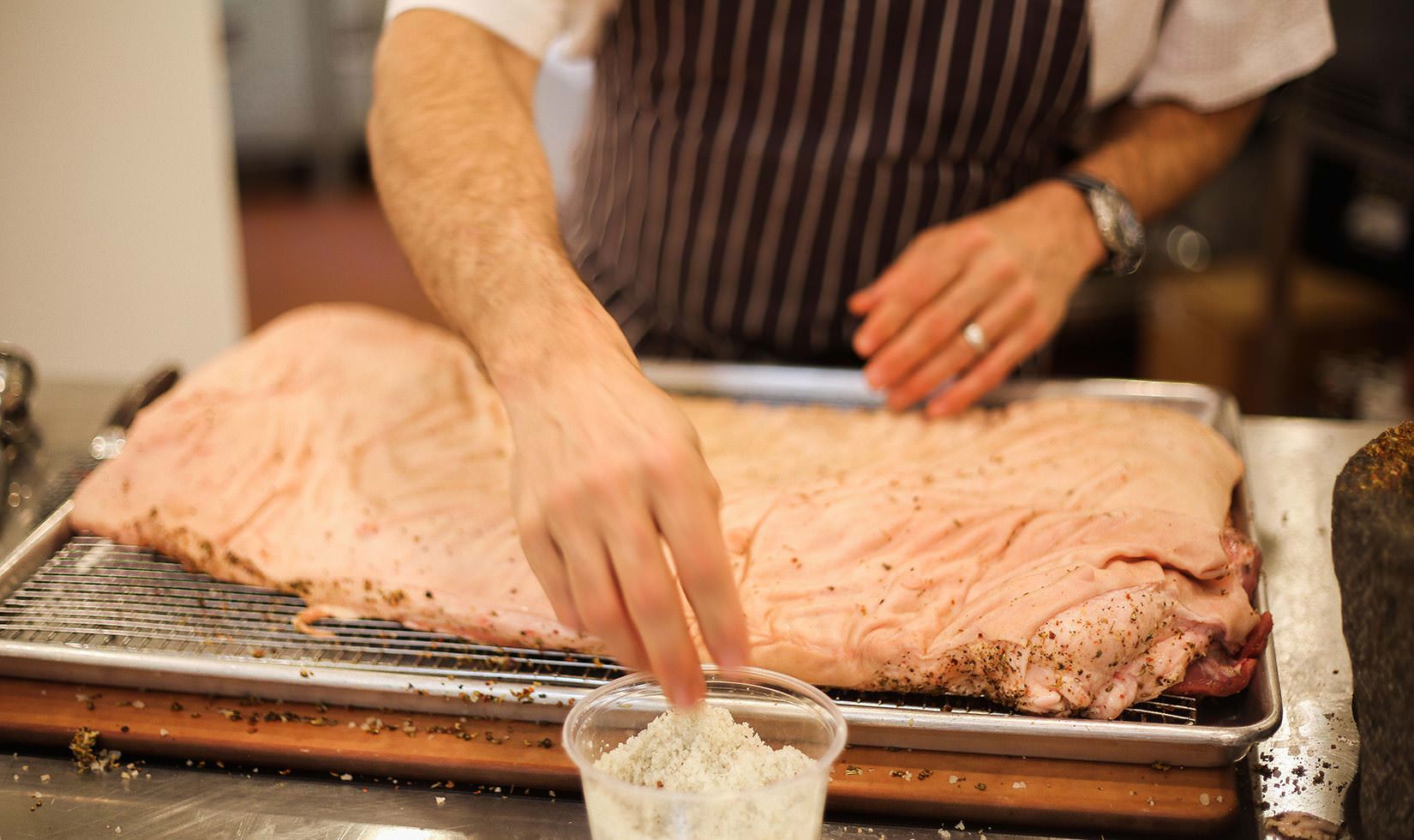 Herb Roasted Pork Belly Porchetta Recipe a person sprinkling the salt and spices