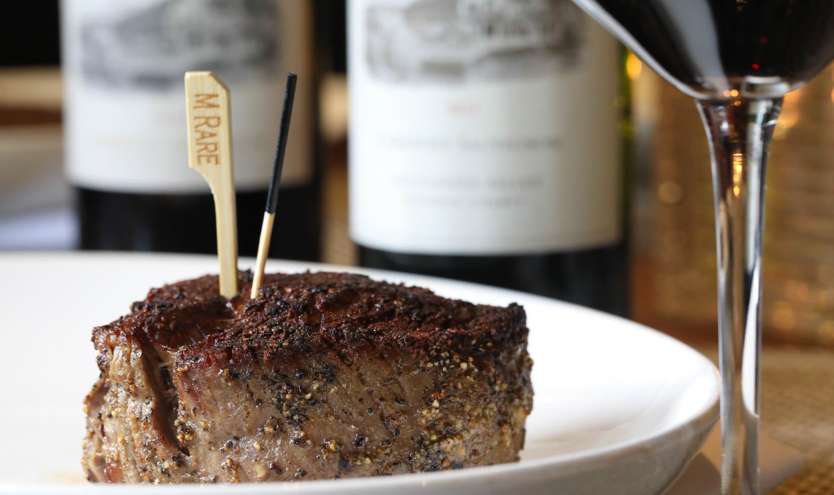 Food Pairing with Cabernet Sauvignon cooked filet mignon on plate next to a glass of Cabernet with bottles of Jordan Winery Cabernet in the background