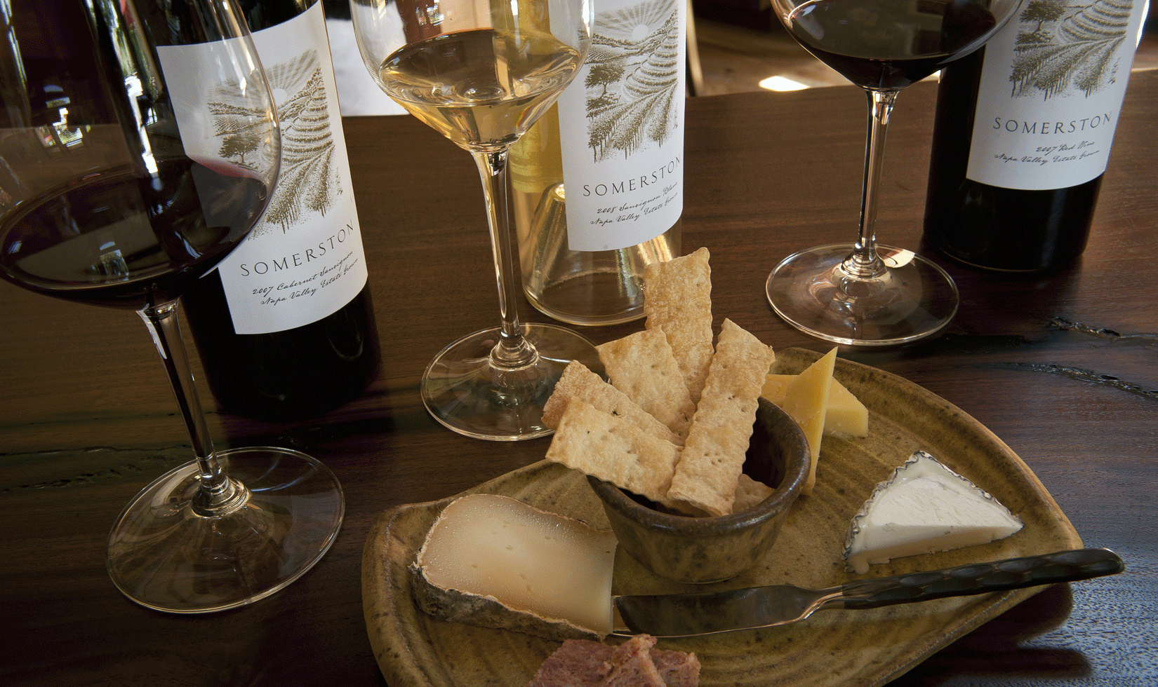 big bottles of wine and wine glasses with a cheese pairing
