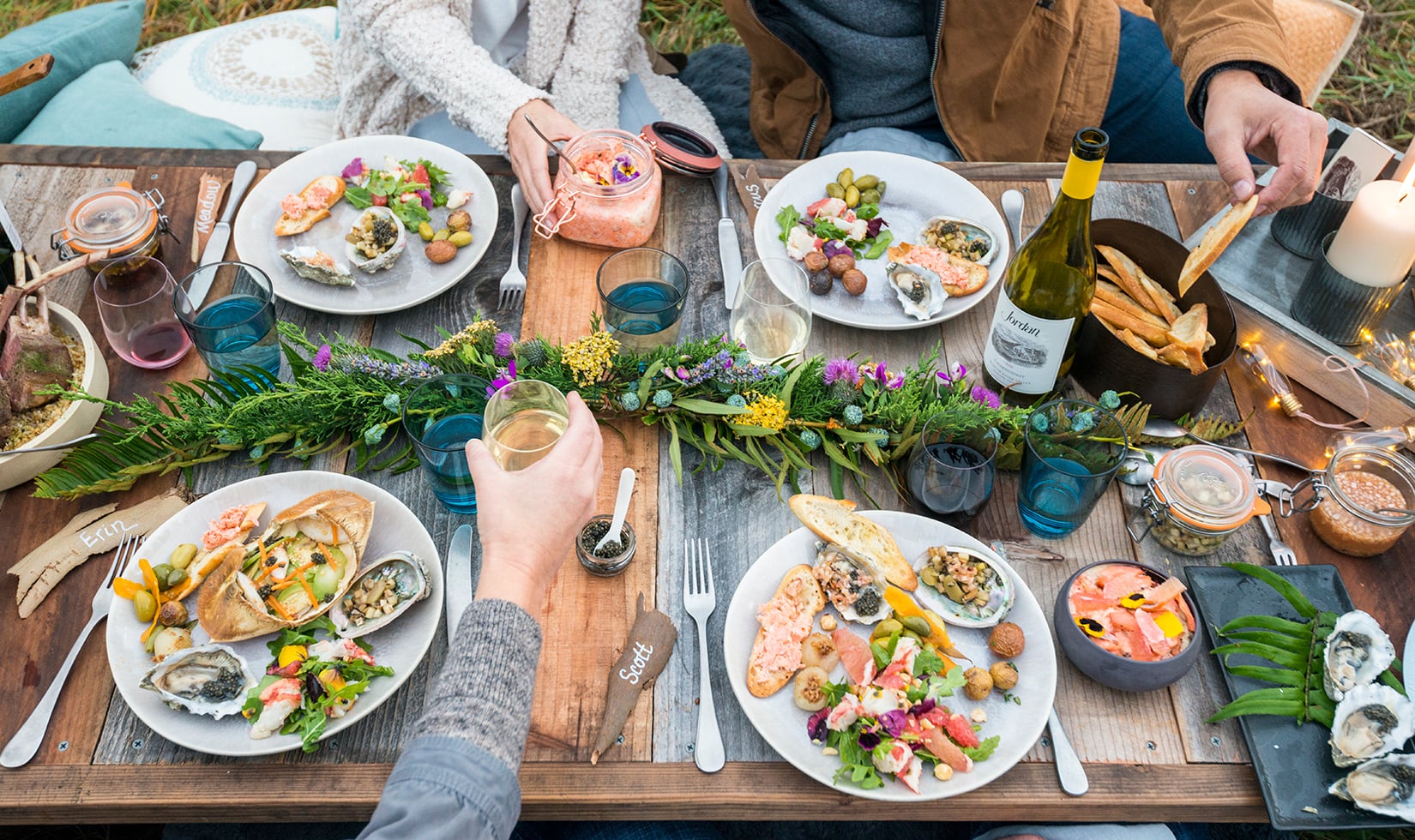 Outdoor seafood feast with wine and vibrant table decor Full plates with crab salad, potatoes, salmon rillette and more at a coastal picnic