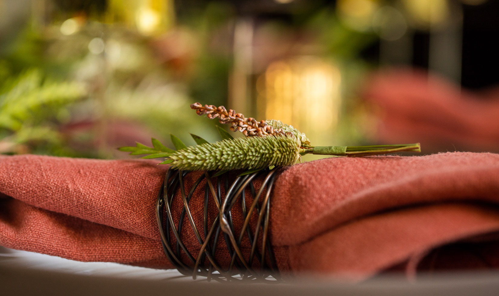 close up of coral napkin with copper napkin ring and sprig of millet