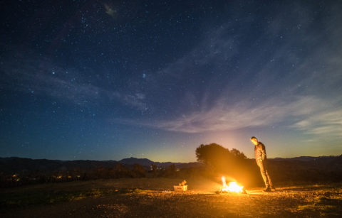 man standing in a field with a fire in front of him
