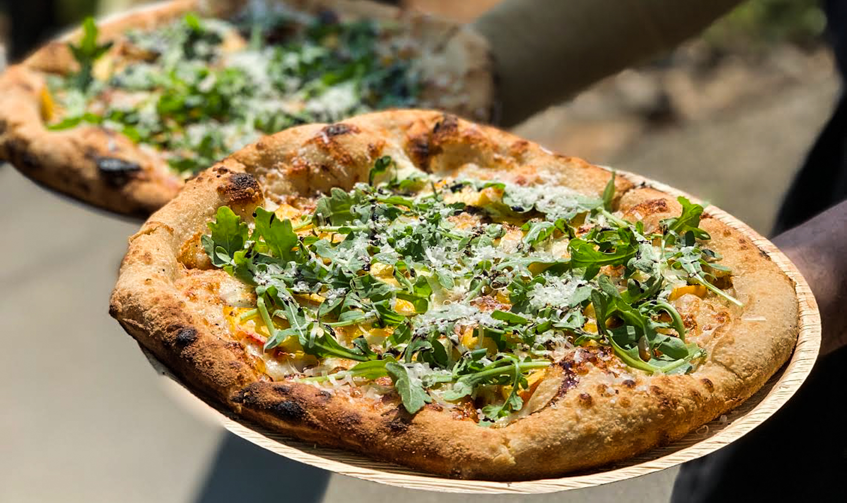 person holding two wood-fired pizzas