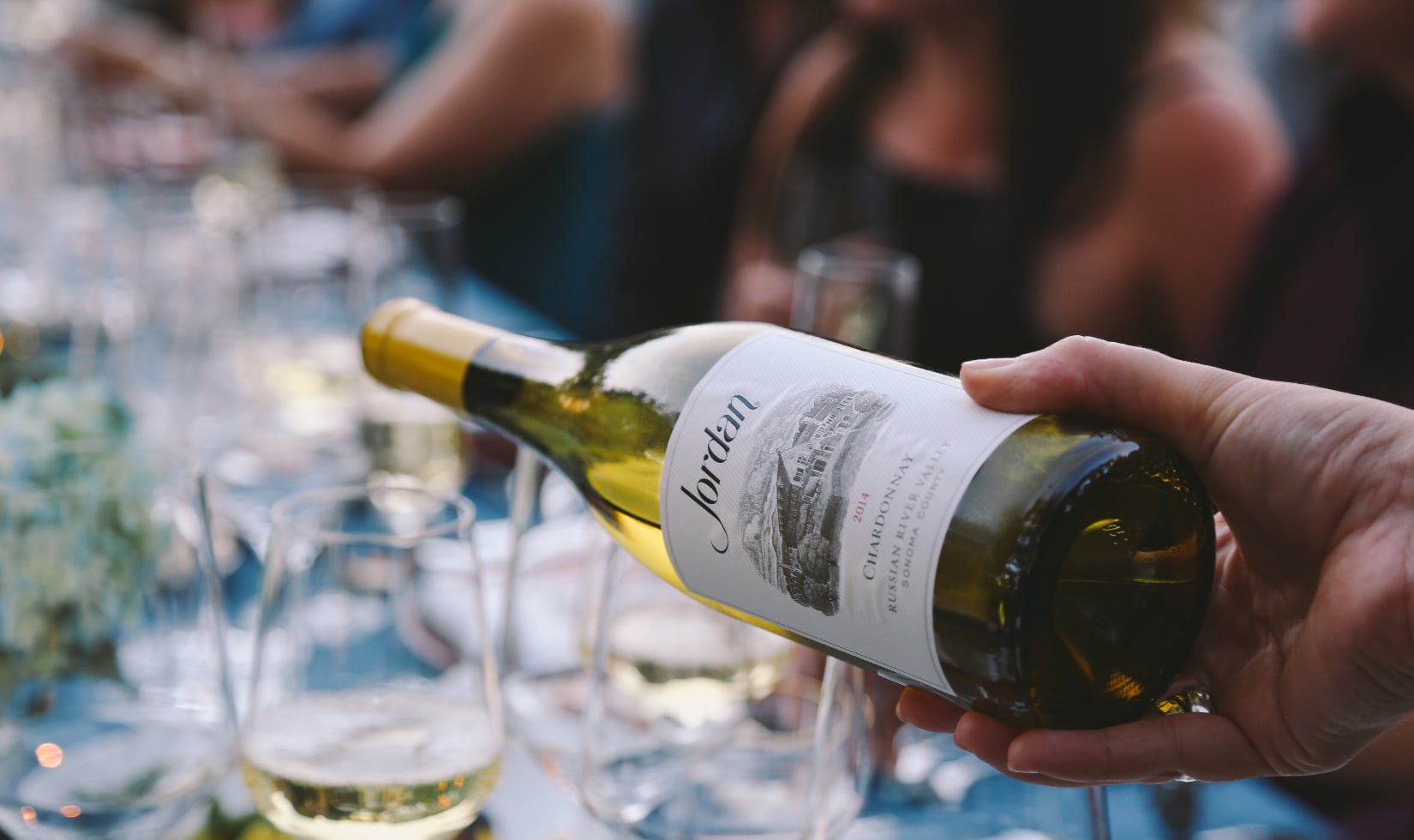 Wine Companies that Donate to Charity Jordan Chardonnay being poured into a glass on an outdoor table decorated with a blue tablecloth and flowers