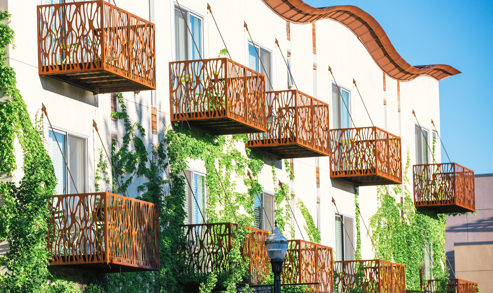Modern building with unique metal balconies and lush greenery.
