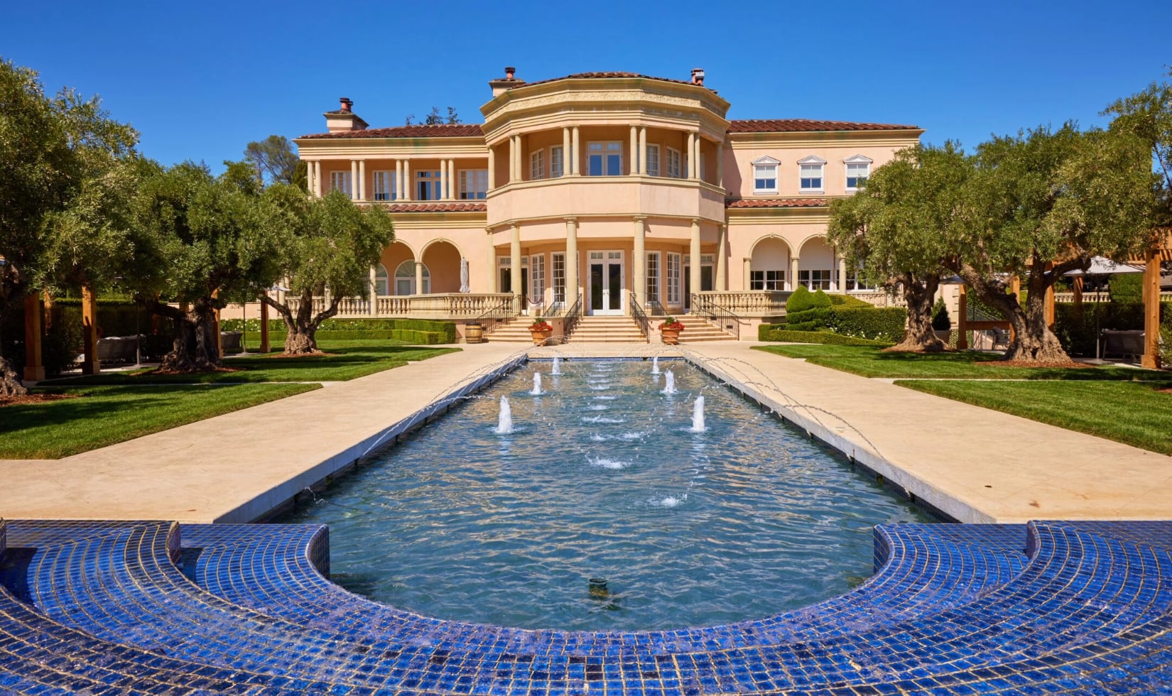 The exterior of the Ferrari -Carano villa with a blue tiled pool with multiple fountains in front of a terrace with columns