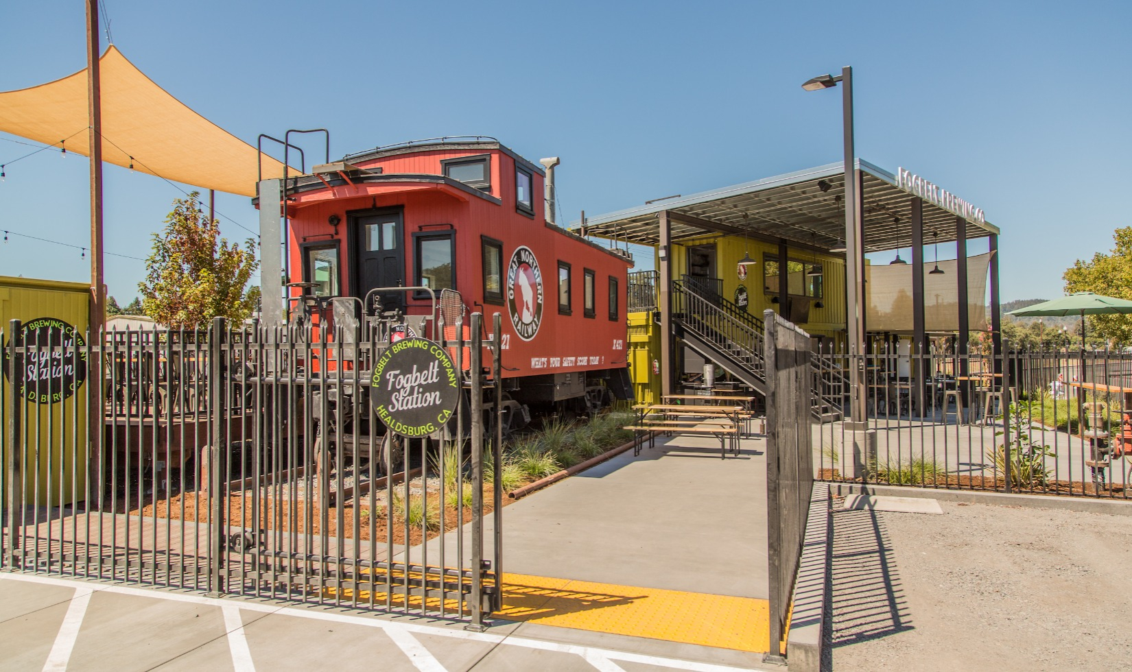 Exterior of Fogbelt station with red train caboose structure next to wooden deck with seating.