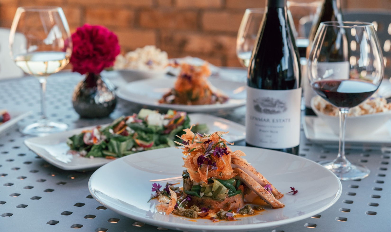 Outdoor table with culinary dishes and glasses of pinot noir and chardonnay.