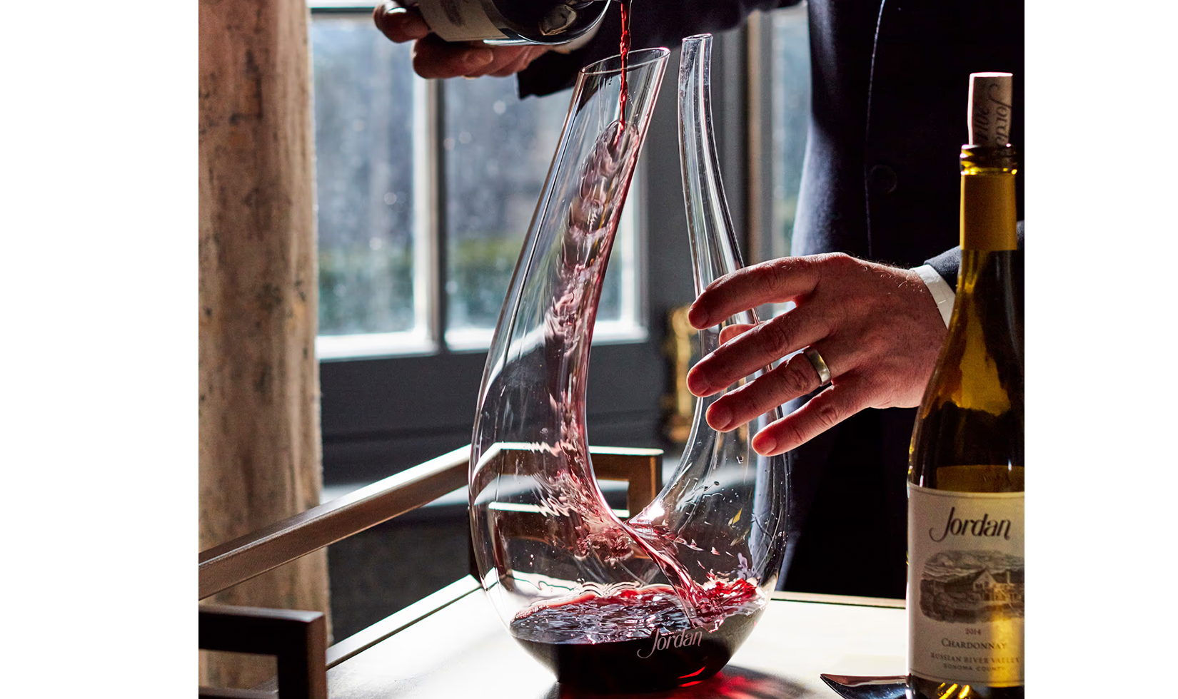 Red wine being poured into a Jordan-branded decanter with a bottle of Jordan Chardonnay nearby.