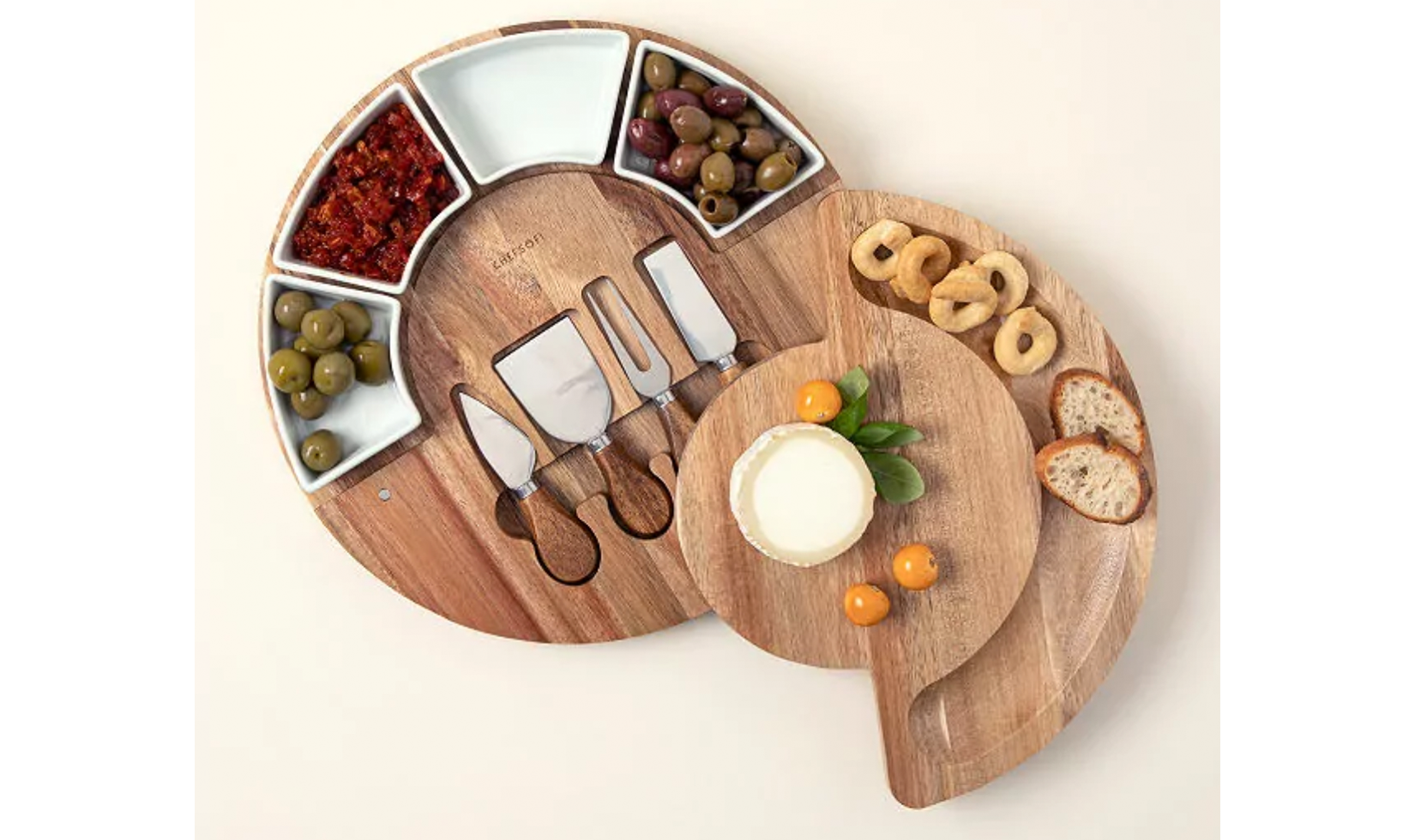 Wooden cheese board set with knives, olives, bread, and cheese.